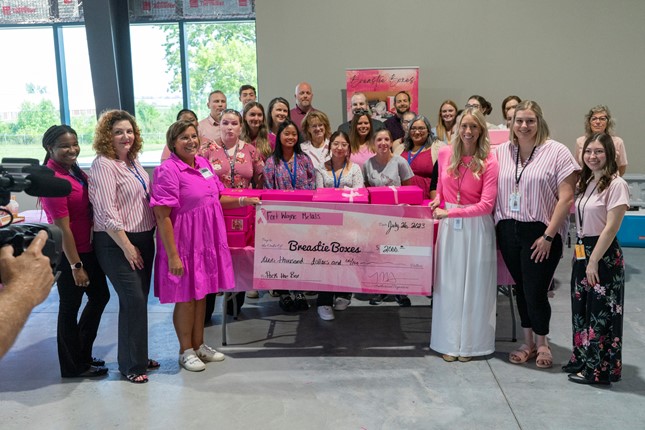 a group of women wearing different shades of pink hold a large donation check for Breastie Boxes